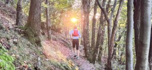 Escursionista percorre un sentiero nel bosco illuminato dal sole, in Ticino.